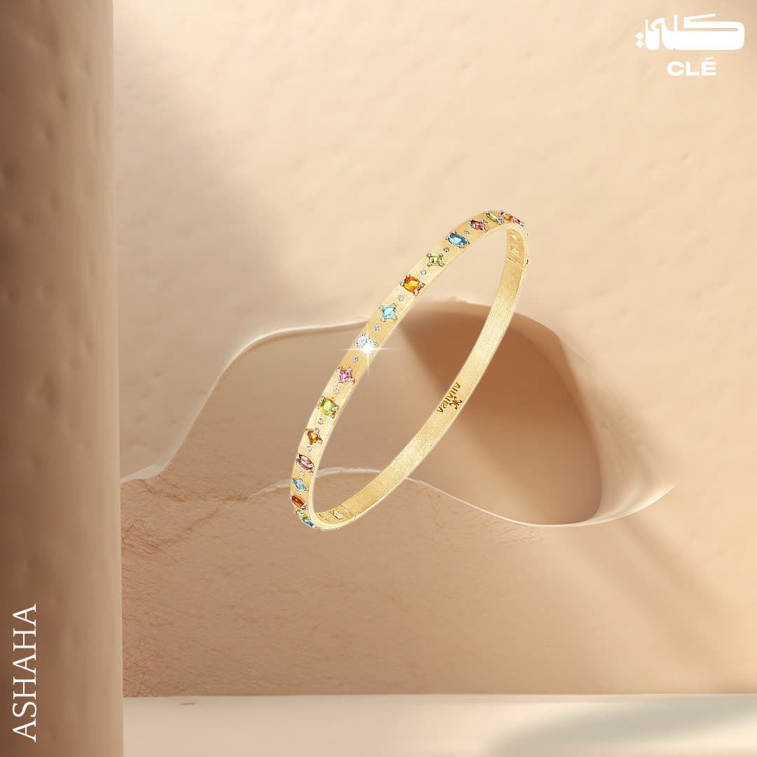 Luxury jewellery design: Gold bangle with coloured gemstones against a sand-toned wall